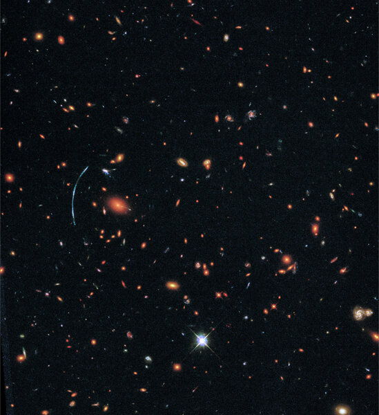 The galaxy cluster SDSS J1110+6459 can be seen here in the as hundreds of galaxies held together by their mutual gravity. The blue arc of the lensed galaxy SGAS J111020.0+645950.8 can be seen on the left.