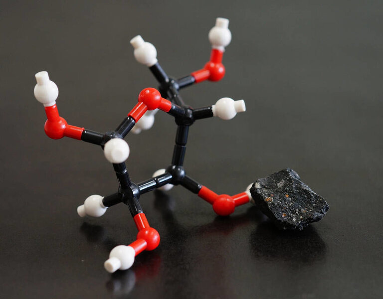 A small piece of the Murchison meteorite (right) with a simple chemical model of ribose, a sugar found in the meteorite. Credit: Yoshihiro Furukawa