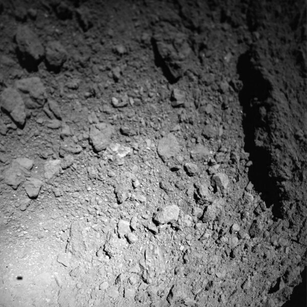 An image from the MASCOT lander as it headed down to the asteroid Ryugu. Note the shadow of the lander to the lower left (this is reversed from the original image to get light source coming from above, so rocks don’t look like pits). Credit: JAXA/DLR/CNES