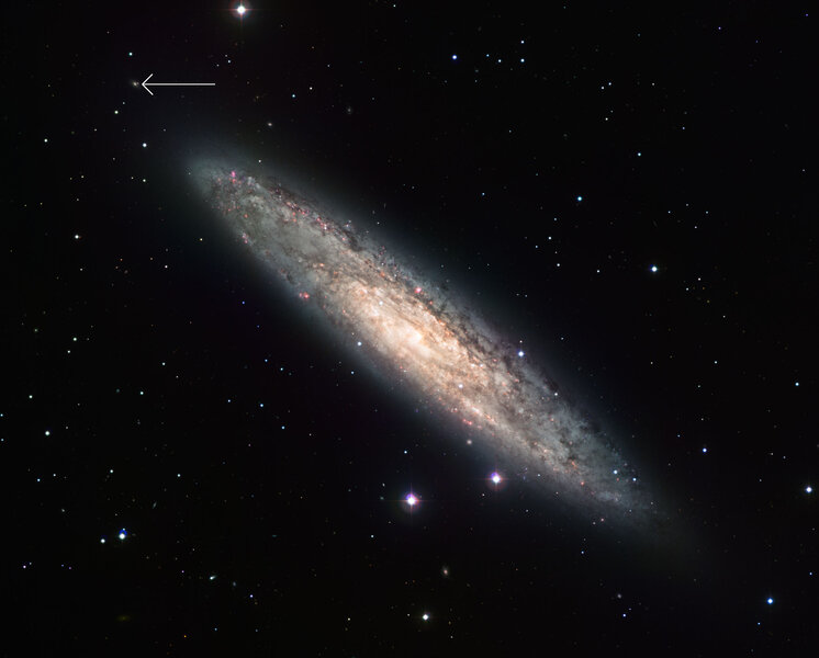 The edge-on spiral galaxy NGC 253 is about 11 million light years from Earth, seen here using the Wide Field Imager camera on the MPG/ESO 2.2-metre telescope. The location of two overlapping background galaxies is arrowed. Credit: ESO