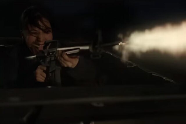 A woman firing a machine gun from a car