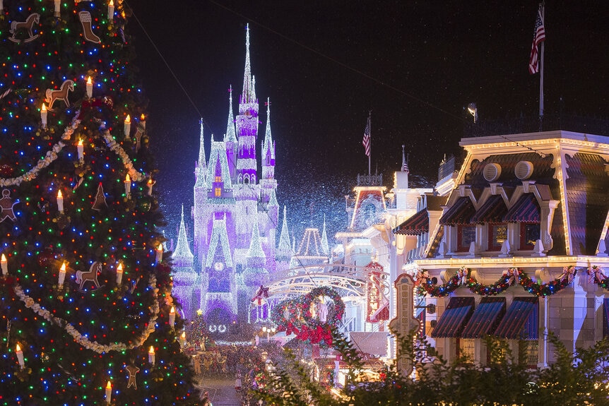 Cinderella Castle covered in lights with a view of Main Street, USA and a Christmas tree in the foreground