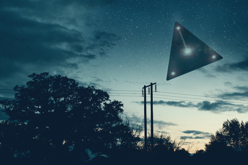 A flying triangle floating above the countryside at night.