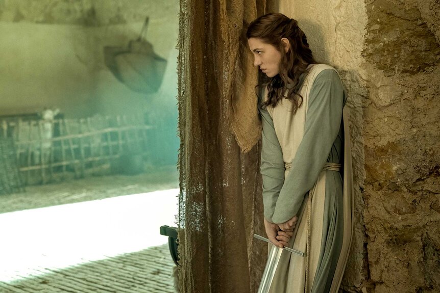 Mathilde Ollivier as Clara holds a sword behind a wall in Mrs. Davis