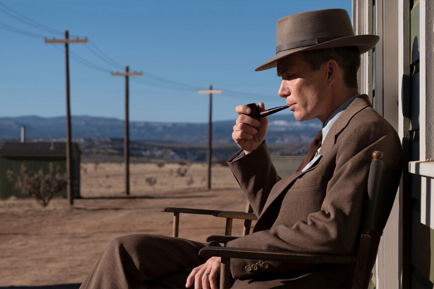 Cillian Murphy as Robert J. Oppenheimer smoking a pipe on a chair outside in Oppenheimer (2023)