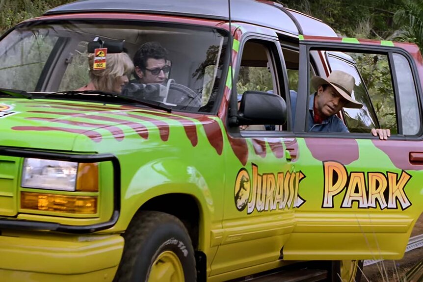Laura Dern and Jeff Goldblum watch as Sam Neill hangs out of a Jurassic Park car