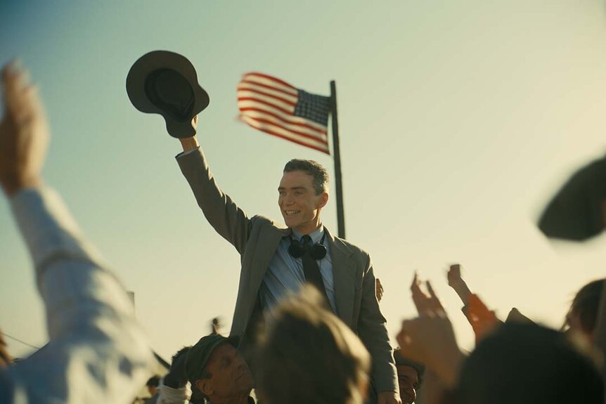 Cillian Murphy waves his hat as an American flag flies in Oppenheimer (2023)