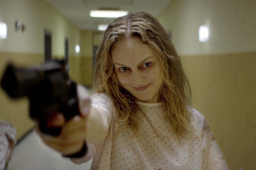 Heather Graham as Elizabeth Derby in a hospital gown points a gun in Suitable Flesh (2023)