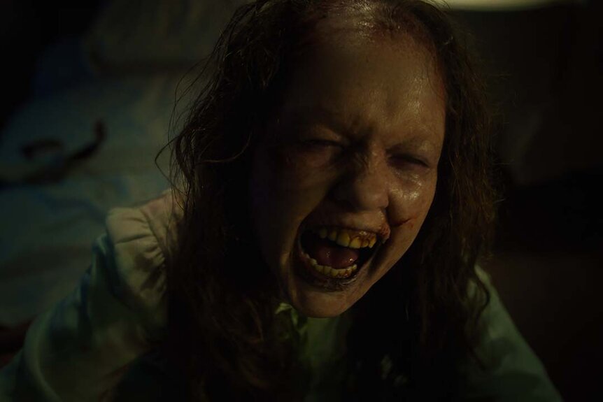 Katherine (Olivia O’Neill) is balding and broken as she laughs/grimace in The Exorcist: Believer (2023).