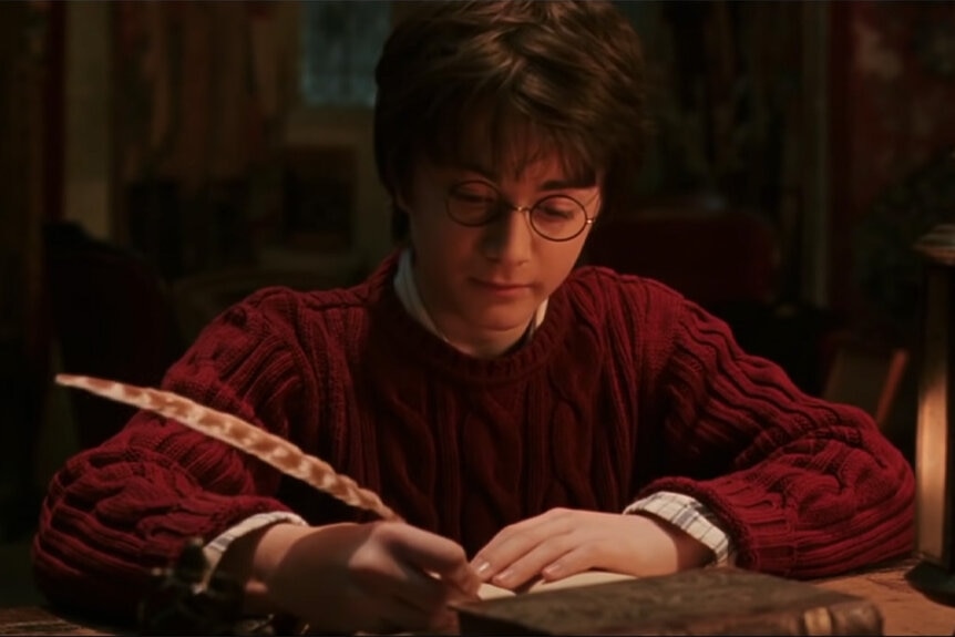 Harry Potter (Daniel Radcliffe) writes with a quill pen in Harry Potter and the Chamber of Secrets (2002).