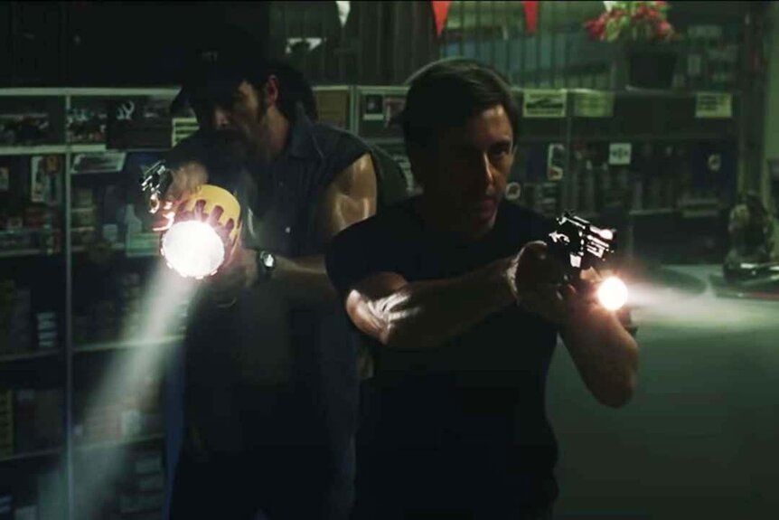 Two men point flashlights and guns in the dark in Dawn of the Dead (2004).
