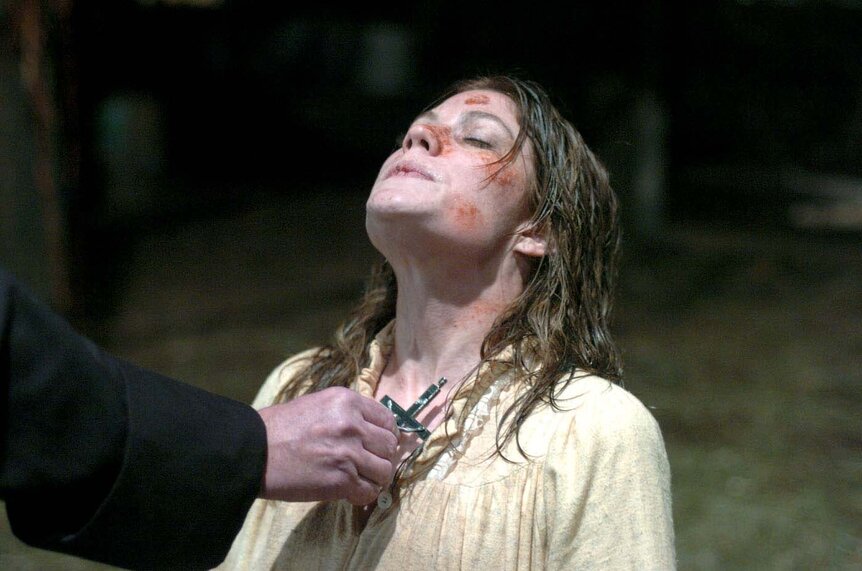 A priest's hand holds a cross to the chest of Emily Rose (Jennifer Carpenter) in The Exorcism of Emily Rose (2005).