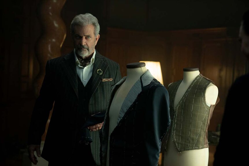 Cormac (Mel Gibson) stands next to suited dress forms in The Continental: From the World of John Wick Night 1.