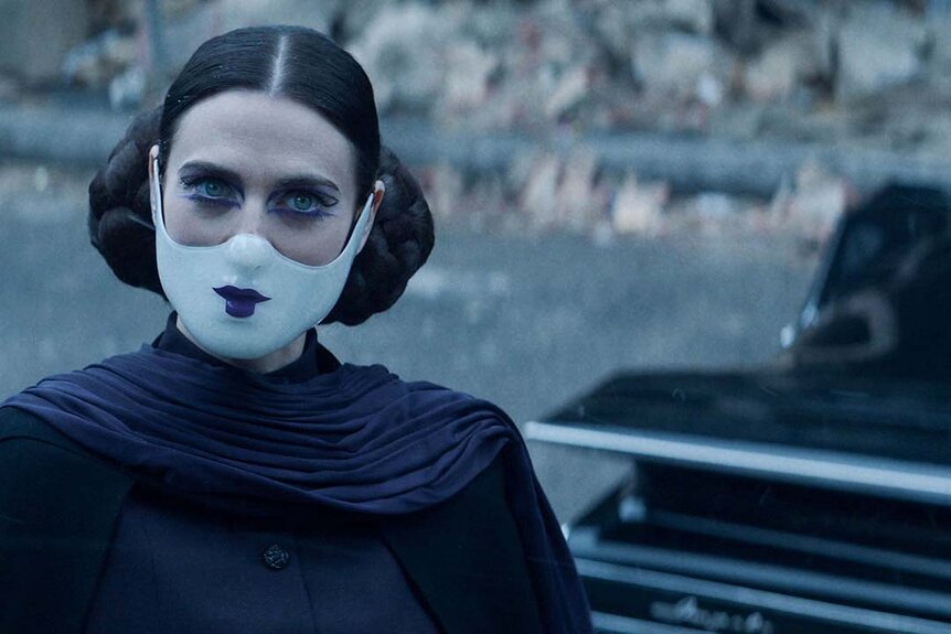Adjudicator (Katie McGrath) wears black with two buns in their hair and a white lower fae mask with painted lips in The Continental: From the World of John Wick Night 3.