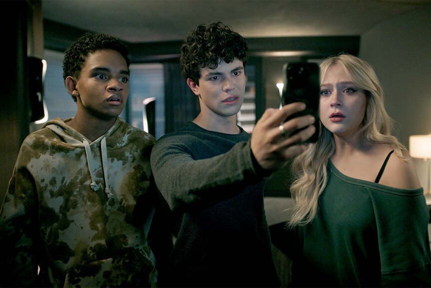 Jake Wheeler (Zachary Arthur) (center) holds a phone up as Devon Evans (Bjorgvin Arnarson) (L) and Lexy Cross (Alyvia Alyn Lind) (R) watch in Chucky 302 -- “Let the Right One In”