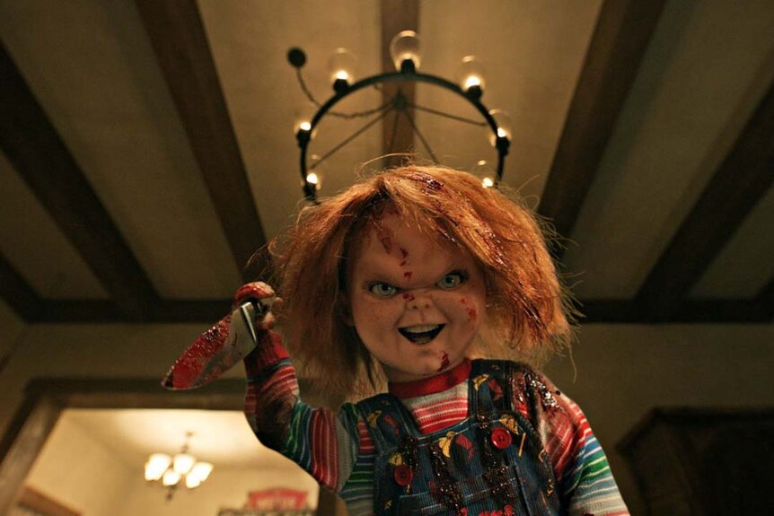Chucky smiles murderously while holding a bloody knife in Chucky 303.
