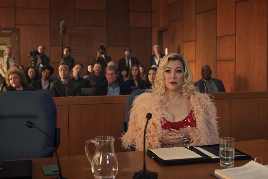 Tiffany (Jennifer Tilly) sits at a prosecutor's table as an audience watches behind her in a courtroom in Chucky 303.