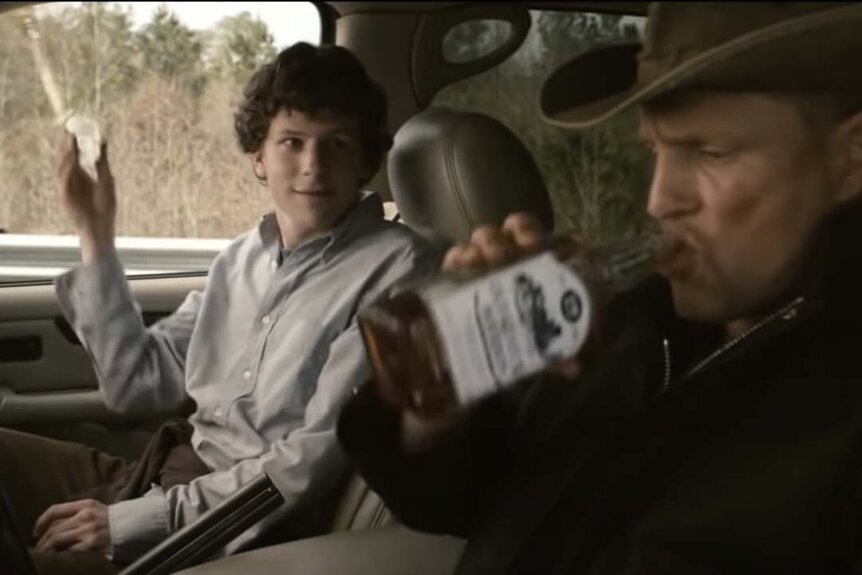 Columbus (Jesse Eisenberg) pours a shot out of the car window as Tallahasee (Woody Harrelson) drinks from a whiskey bottle in Zombieland (2009).