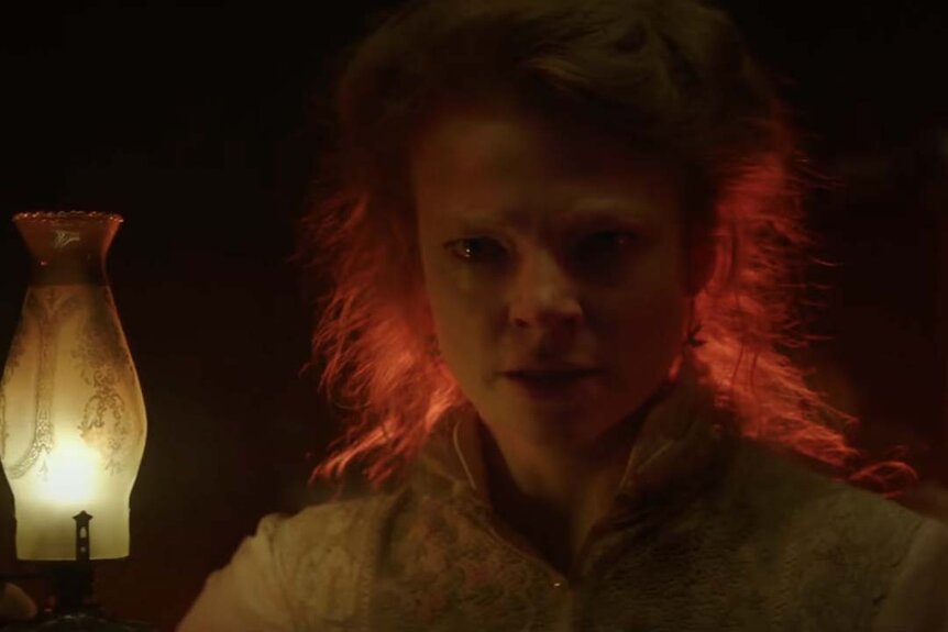 Marion Marriott (Sarah Snook) looks frazzled while holding an oil lamp in Winchester (2018).