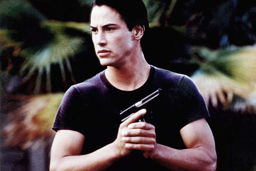 Johnny Utah (Keanu Reeves) holds a gun close to his body in Point Break (1991).