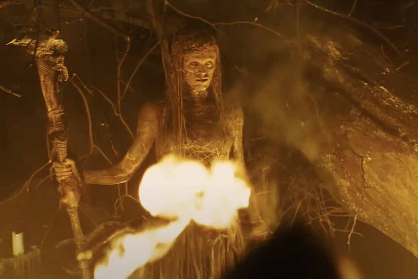 A disheveled witch creature holds a staff in front of a destructive fire in The Last Witch Hunter (2015).