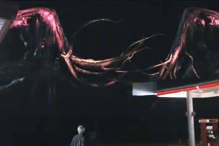 Giant red squid-like monsters float in the sky as a person watches from below.