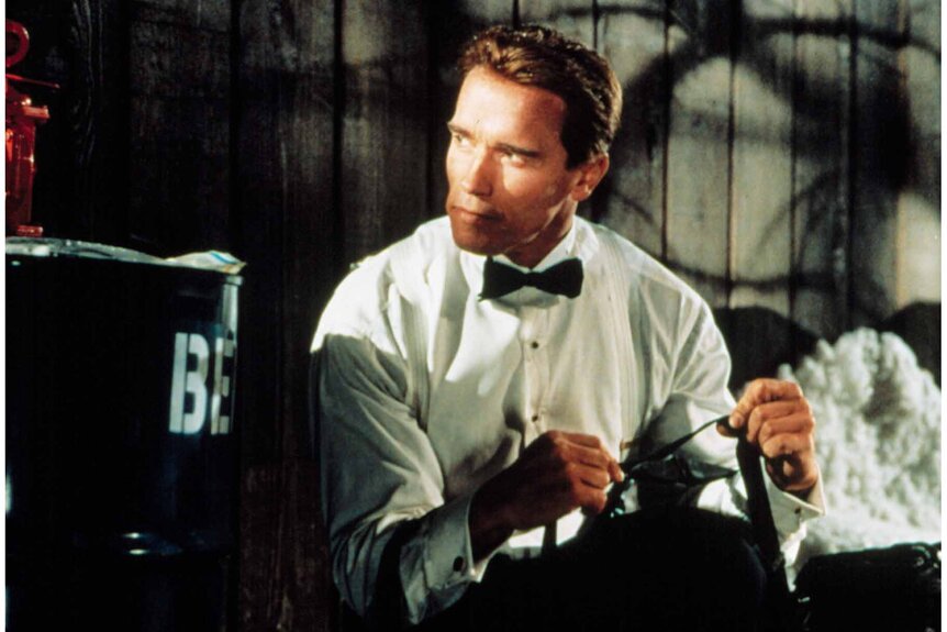 Harry Tasker (Arnold Schwarzenegger) in a white dress shirt and black bowtie in True Lies (1994).