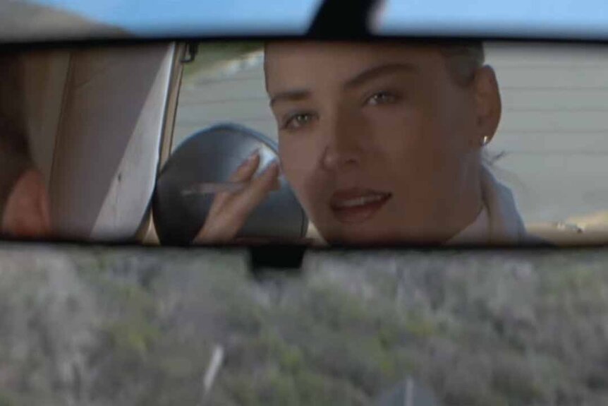 Catherine Tramell (Sharon Stone) smokes a cigarette in a car's rearview mirror in Basic Instinct (1992).