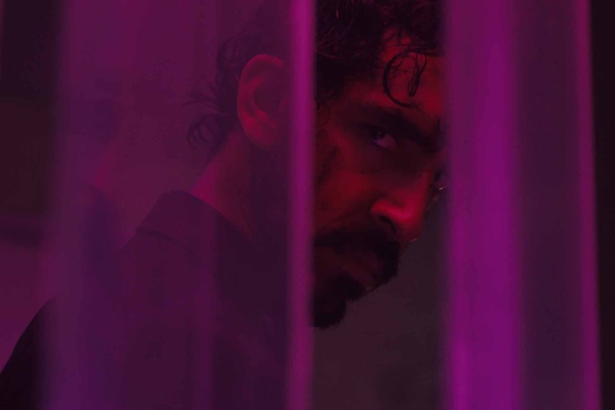 Dev Patel gazes through purple curtains in Monkey Man (2024).