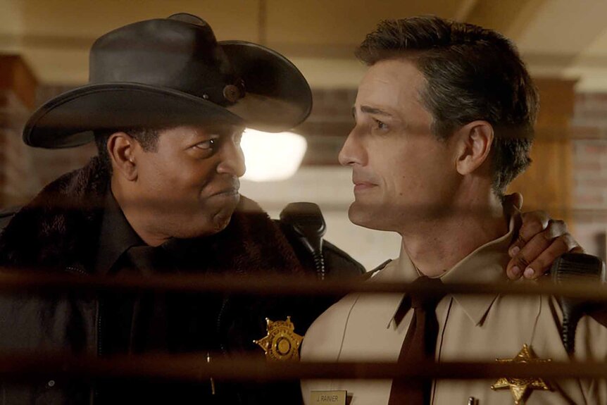 Sheriff Mike Thompson and Joseph Rainier are seen look at each other through blinds in Resident Alien Episode 301.