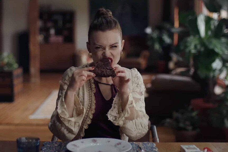 Anya (Holland Roden) bites into a brownie in Mother, May I? (2023).