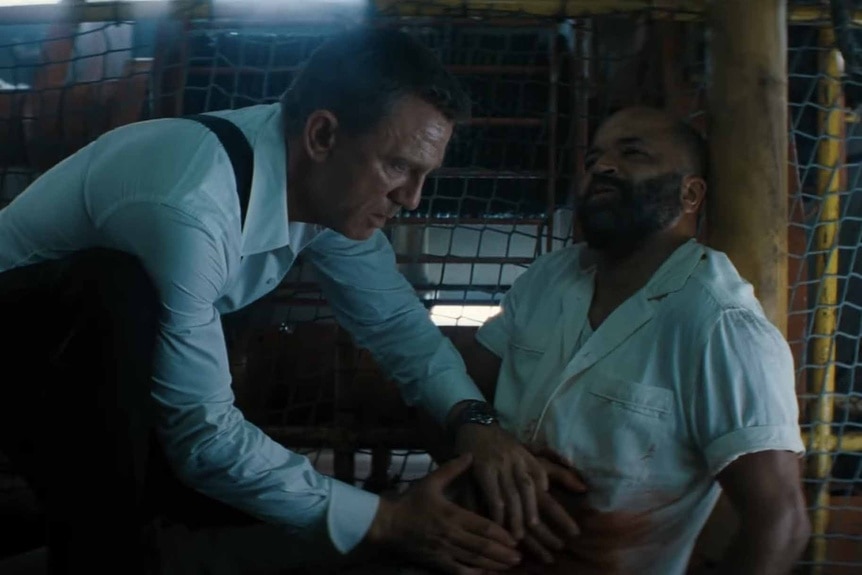 James Bond (Daniel Craig) tends to a wounded Felix (Jeffrey Wright) in No Time to Die (2021).
