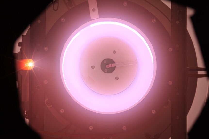An air-breathing thruster glows pink as an ionized nitrogen-oxygen gas mix is accelerated out the back, providing thrust. Credit: ESA/Sitael