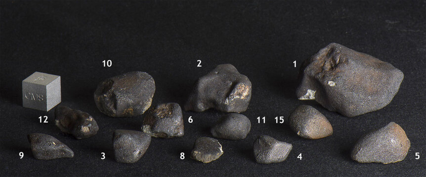 A dozen of the Dishchii’bikoh meteorites collected in Arizona. The cube on the left is for scale, and is one centimeter on a side (the size of a normal six-sided die). Credit: Jenniskens et al.