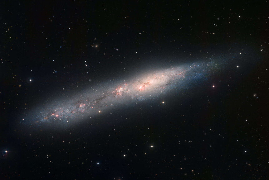 NGC 55, a nearly edge-on dwarf spiral galaxy, seen using the MPG/ESO 2.2-meter telescope in La Silla, Chile. This image is closer to true color, with gas clouds showing as red. Credit: ESO