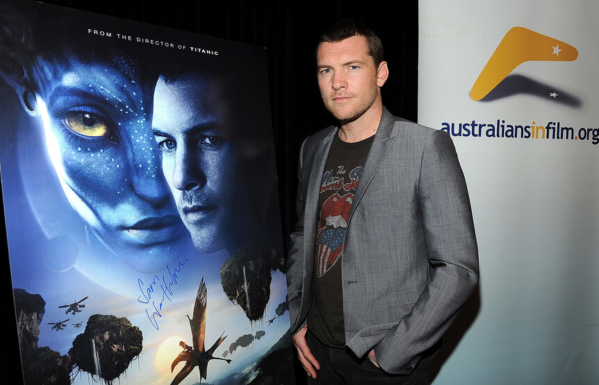 Lead actor Sam Worthington standing in front of a poster for the movie Avatar