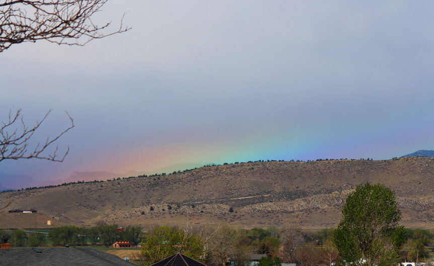 The very tippy top of a rainbow peeks out above the Colorado Rocky Mountain foothills. Credit: Phil Plait