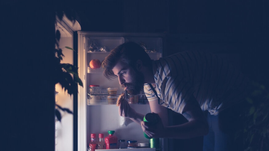 Man having snack in front of the refrigerator at night.