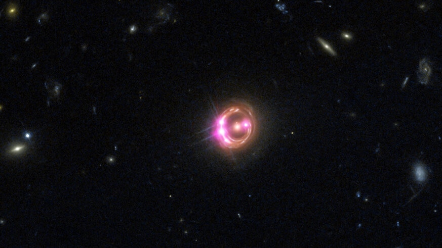 The quasar RX J1131-1231 appears as a series of bright dots on a ring around the fuzzy elliptical galaxy in the center due to gravitational lensing. This is a Hubble image (red, green, and blue) combined with Chandra which sees X-rays (displayed as pink).