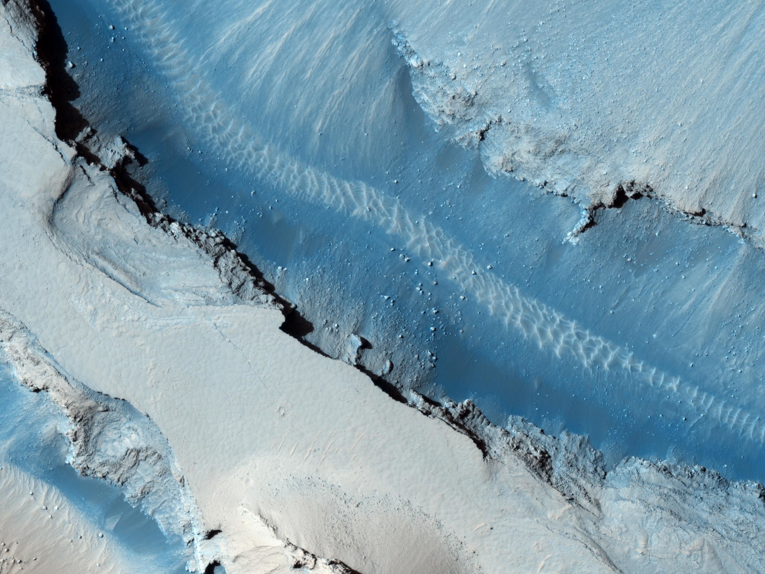 Sand dunes ripple across the floor of a graben in Cerberus Fossae on Mars in this enhanced color image (Mars is dark grey and ochre, not blue). Credit: NASA/JPL-Caltech/University of Arizona