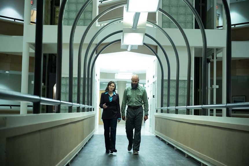 (l-r) August Ripley (Maurice Dean Wint) and Rochelle (Joy Tanner) walk down an arched indoor walkway in SurrealEstate 205.