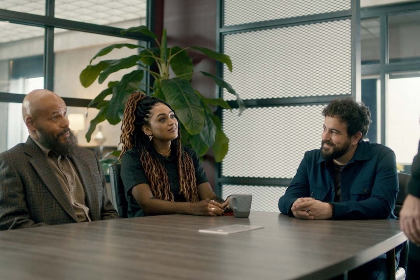 (l-r) August Ripley (Maurice Dean Wint), Zooey L'Enfant (Savannah Basley), and Father Phil Orley (Adam Korson) sit a a large table